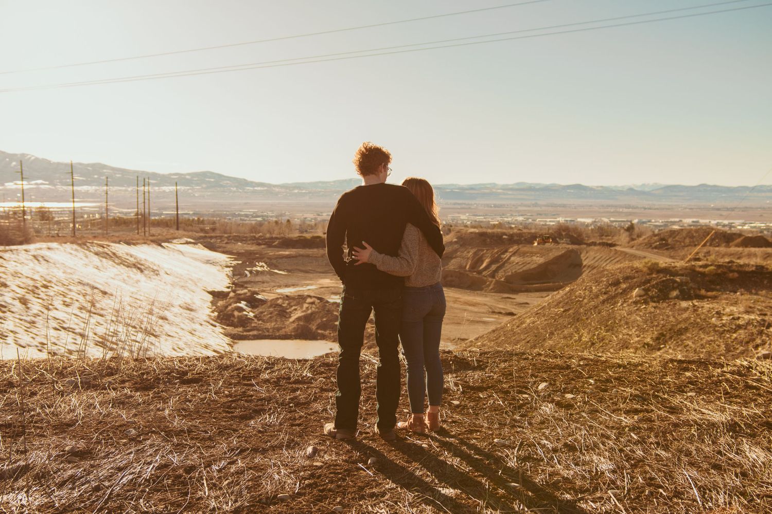 Silhouettes of couple standing together against vast desert landscape at sunset.