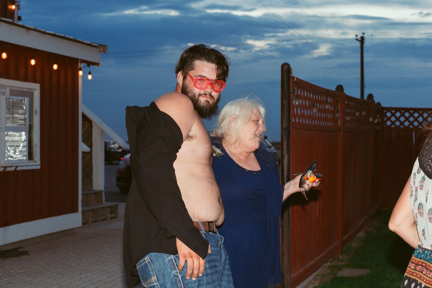 Wedding guests dance under string lights at dusk with a red barn in the background.