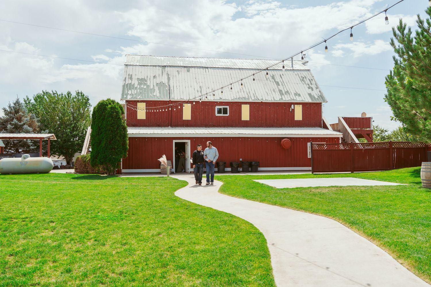 Red barn venue with string lights and a concrete path leading to the entrance on a cloudy day.