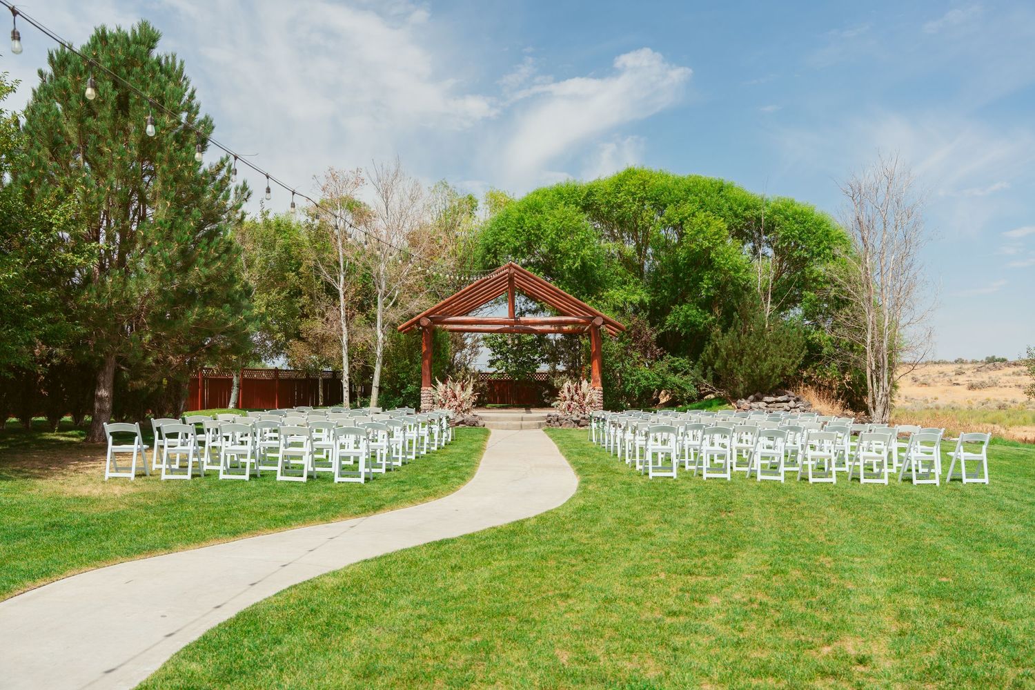 Rows of white chairs set up for an outdoor ceremony with a rustic red barn in the distance.