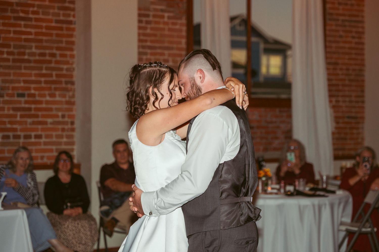 Dancers perform an elegant dip move on a wooden dance floor in a brick-walled reception venue.