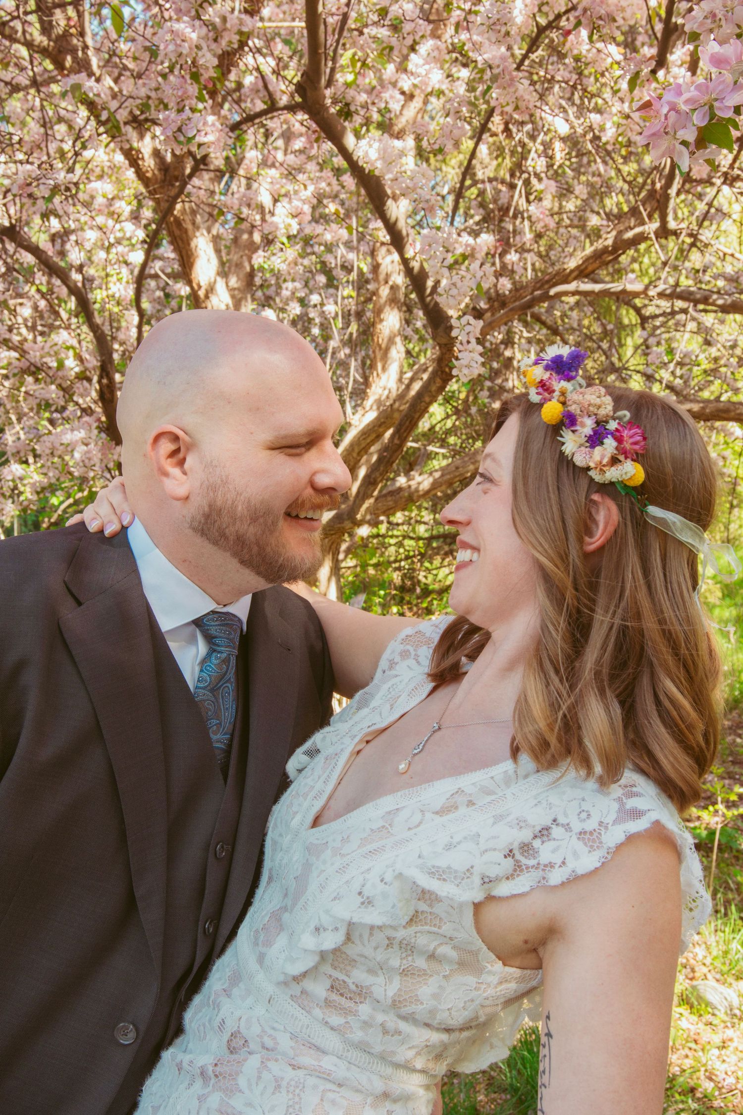 A romantic wedding couple shares intimate moments under blooming cherry blossom trees in springtime.