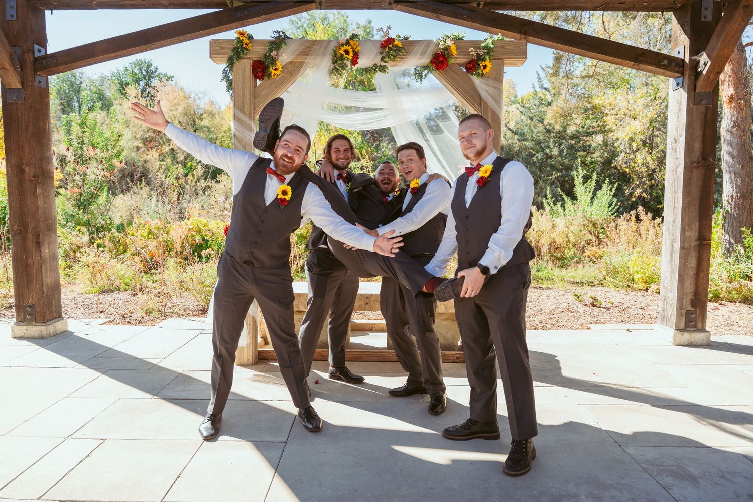Wedding party members strike fun poses under outdoor pavilion decorated for autumn.
