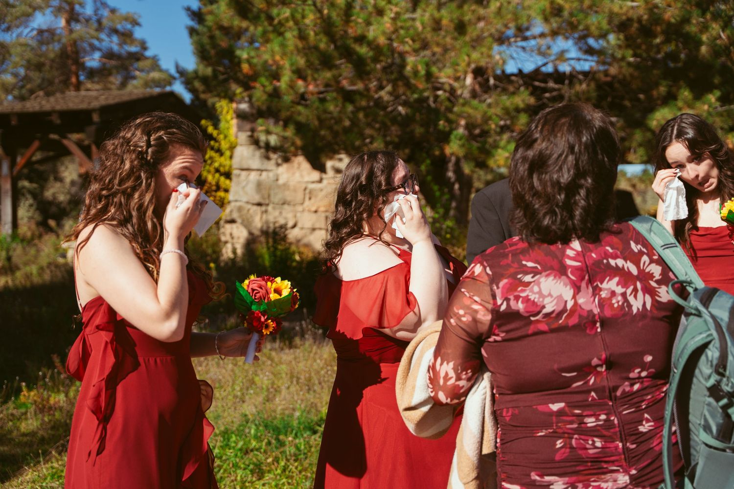 Wedding party members in red dresses and black suits pose together on sunny autumn day.