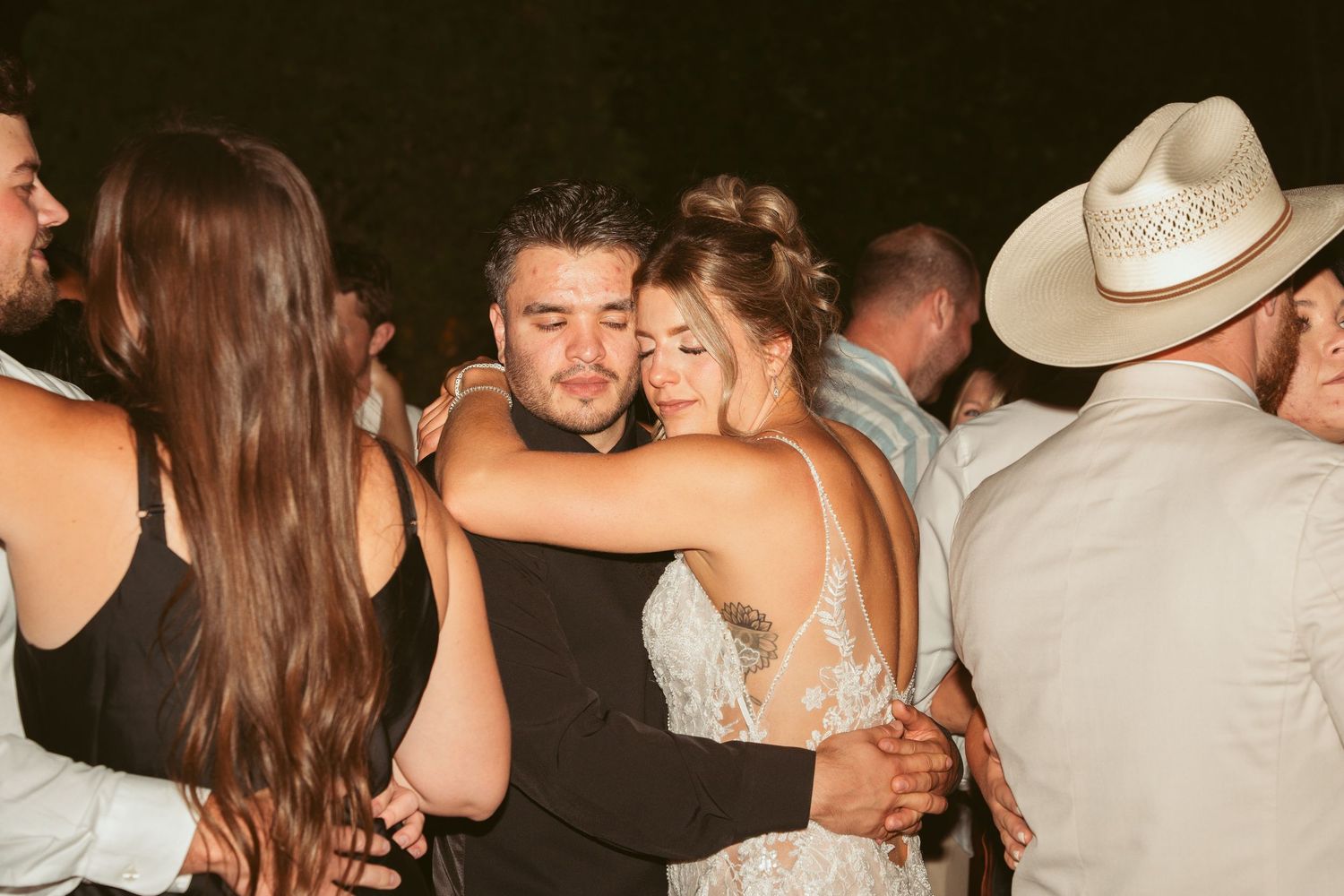 Couples dancing closely together at a wedding reception with someone wearing a cowboy hat.