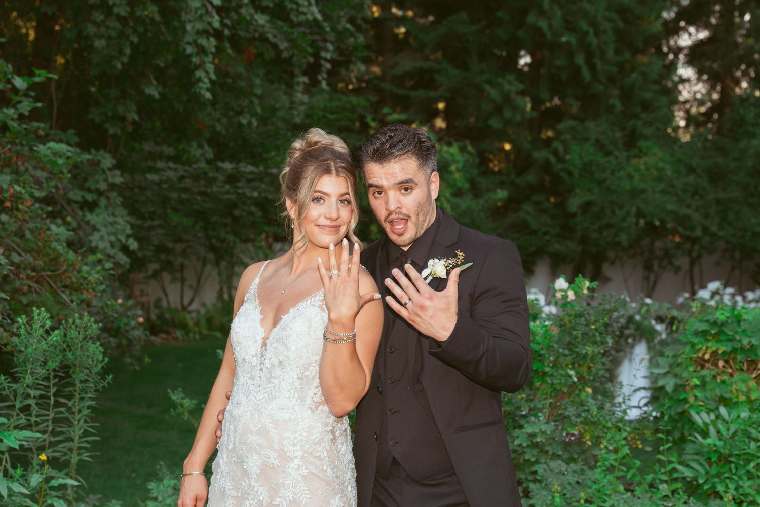 A couple shares an intimate moment in formal attire while standing in a lush garden setting at sunset.