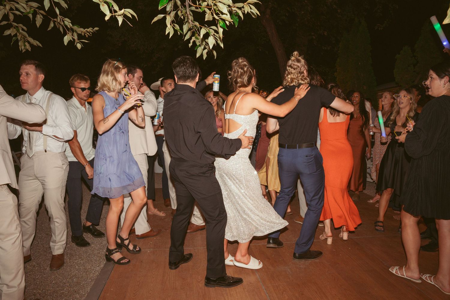 Wedding guests dancing together on outdoor dance floor during evening reception.