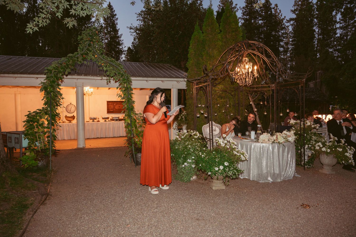 Evening wedding reception setup with string lights and floral decorations in a garden setting.