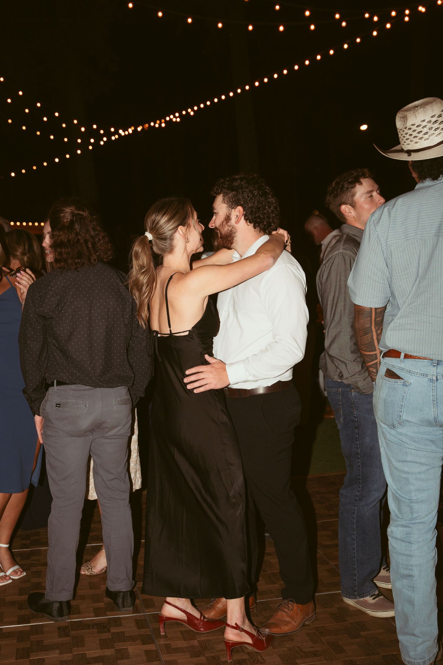 Couples dancing under string lights at an outdoor evening celebration.