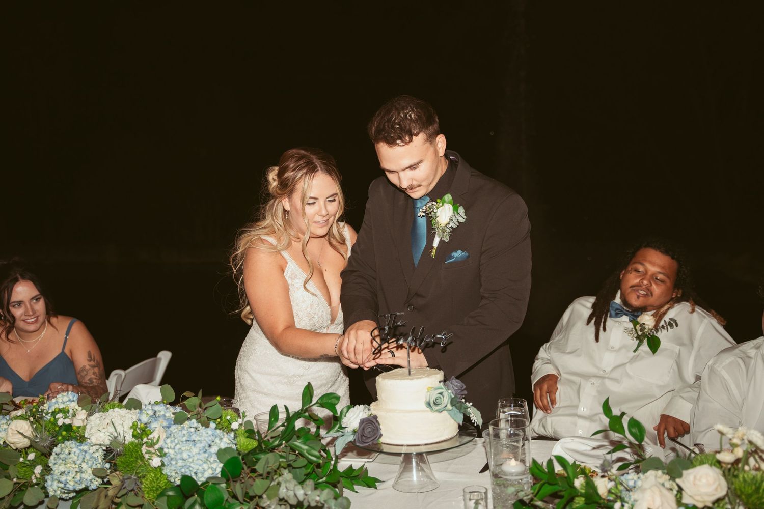Wedding reception guests enjoy dinner at elegantly decorated tables with blue hydrangea centerpieces.
