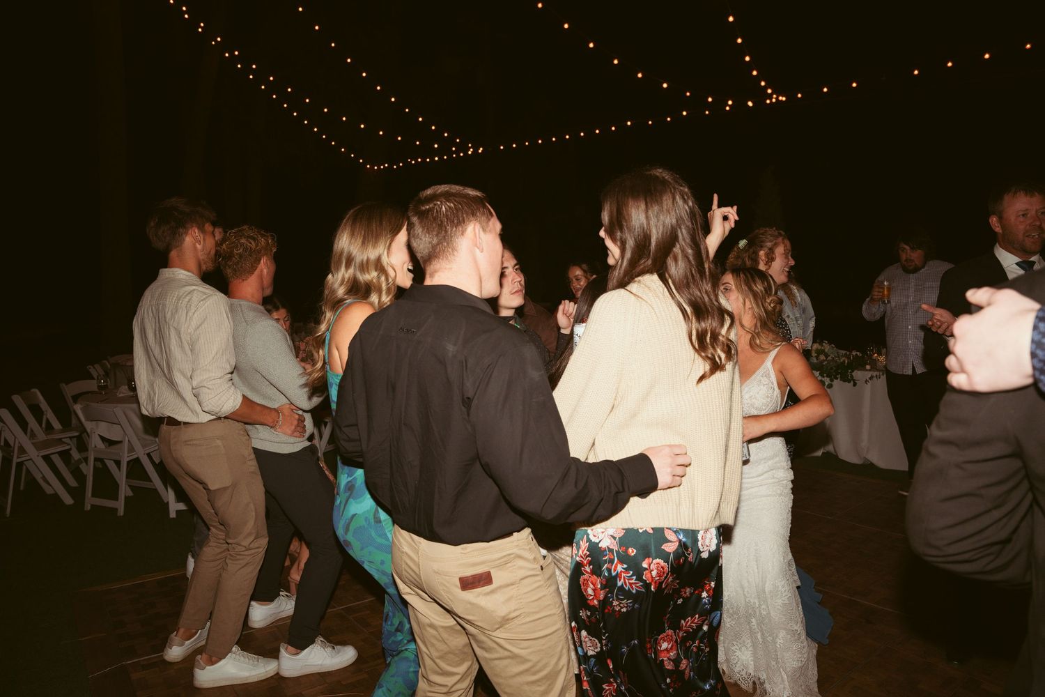 Couples dancing together at a nighttime reception with string lights overhead.