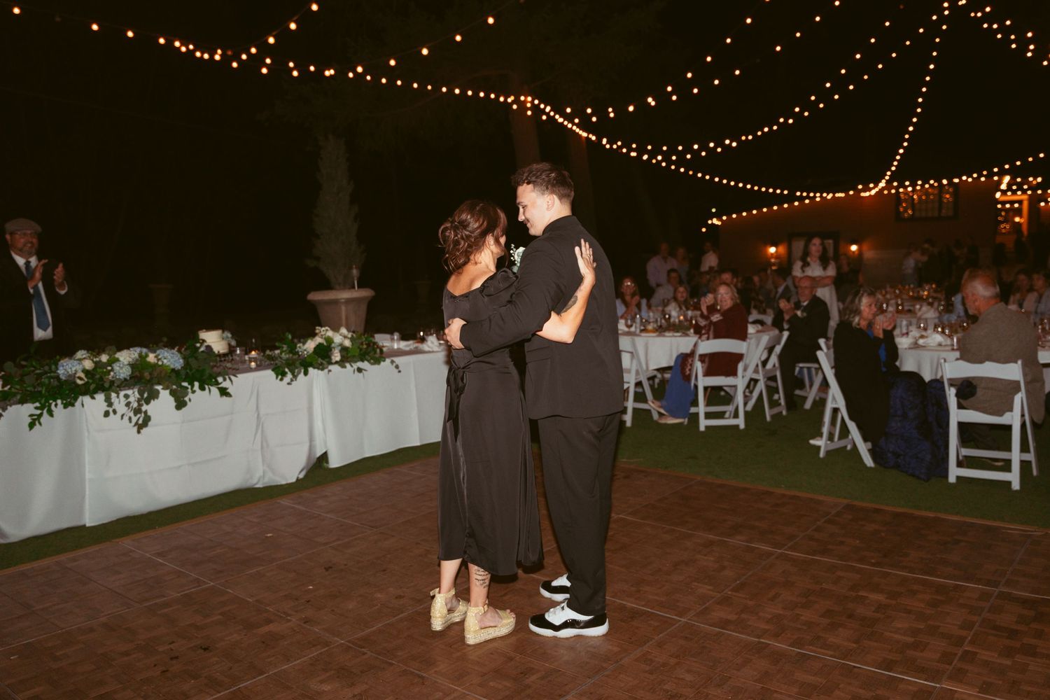 Wedding guests dancing together at a nighttime outdoor reception under string lights.
