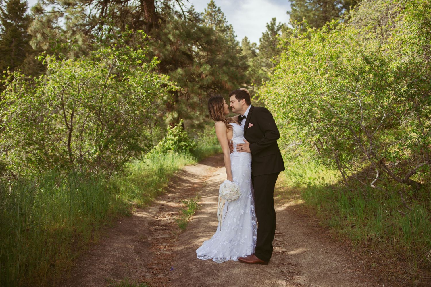 A romantic wedding portrait on a sunlit forest trail.