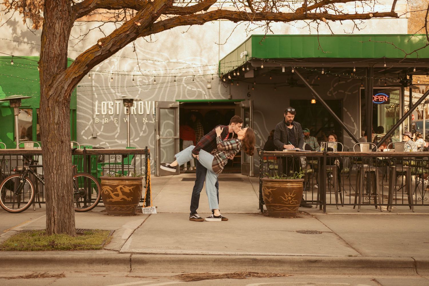 Two people dance outside a casual outdoor dining area with bikes parked nearby.