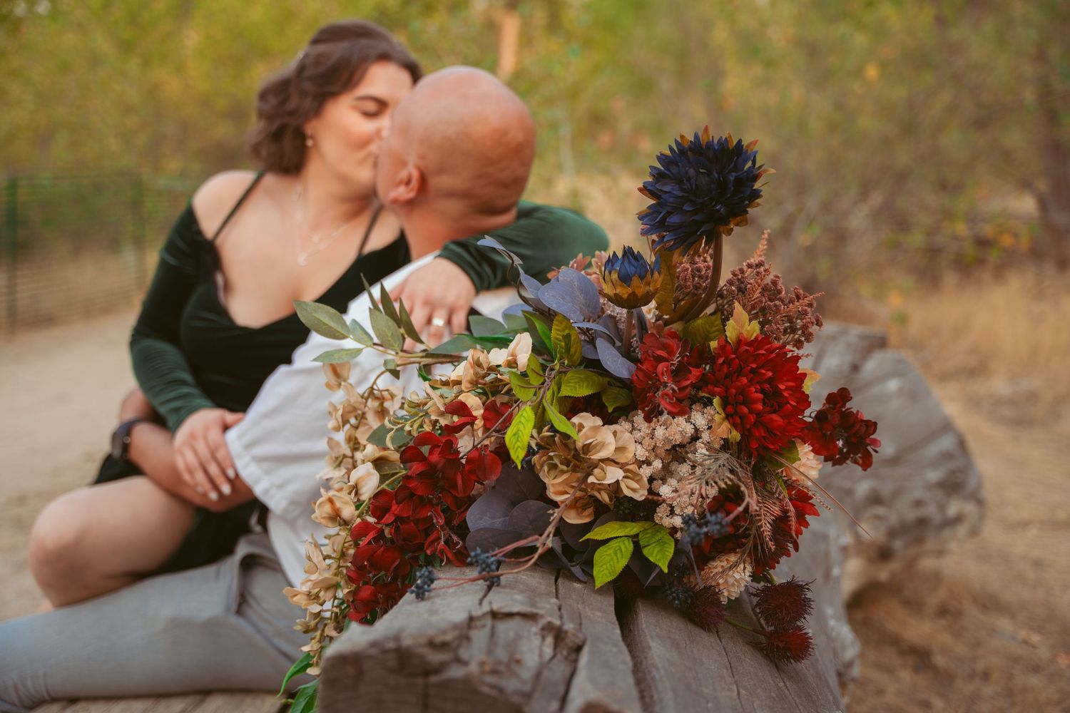A couple embracing with fall-colored flowers in the foreground during a romantic outdoor moment.