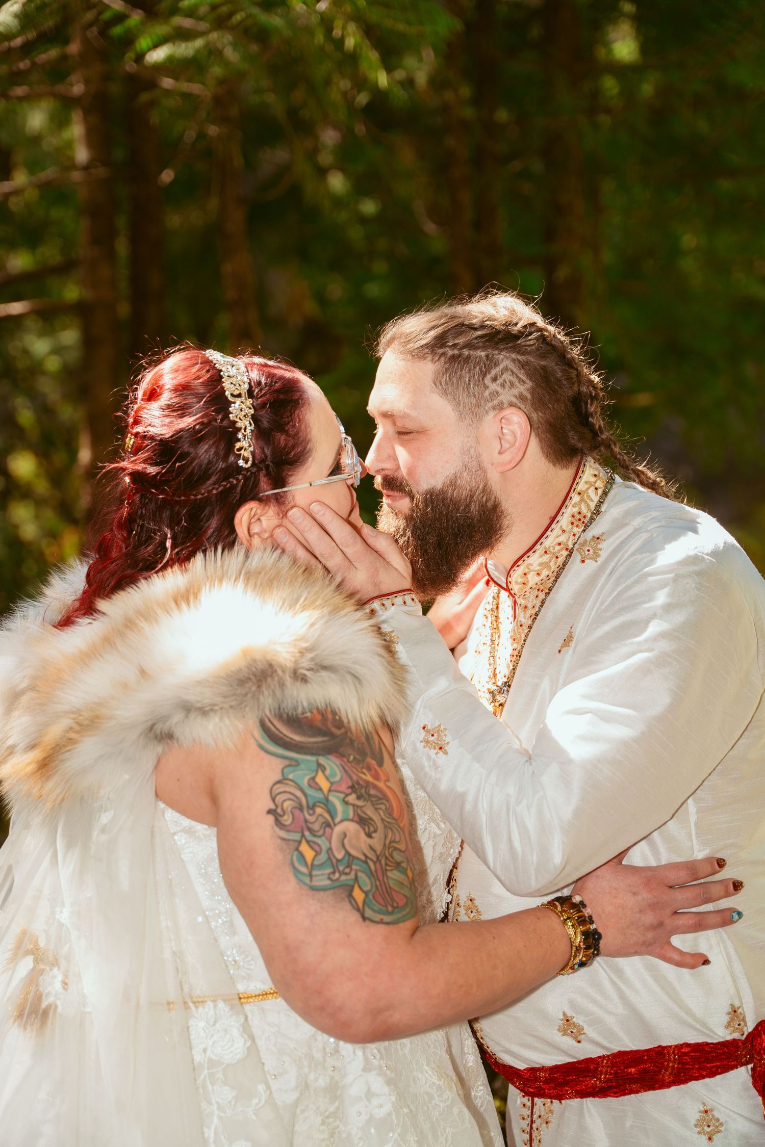 A couple in medieval-inspired wedding attire share an intimate moment in a forest setting.