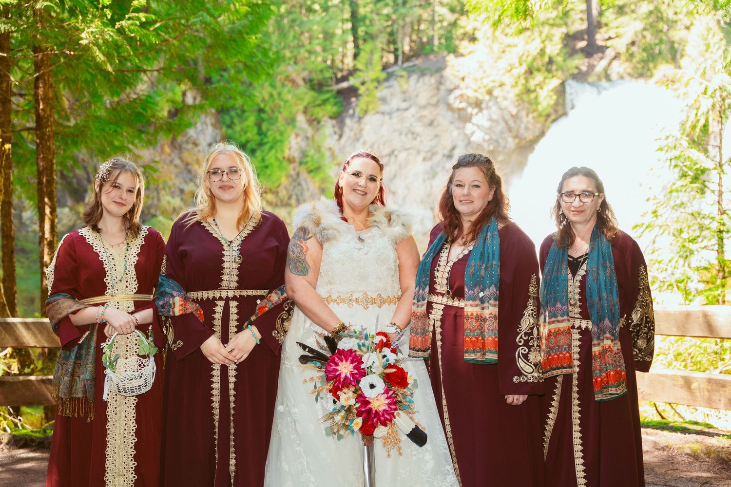 Wedding party members in burgundy medieval-style dresses line up for a forest photo.