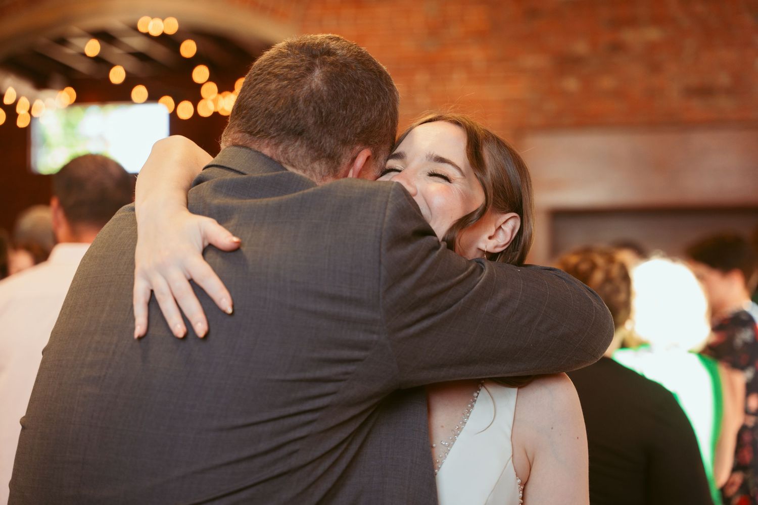 Emotional embraces shared during wedding reception in a warmly lit brick venue.
