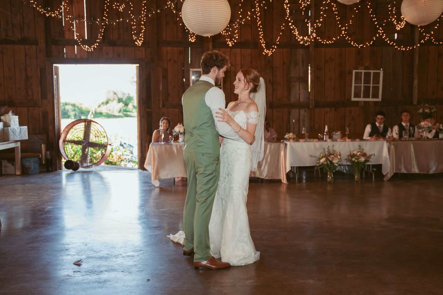 Guests enjoying a wedding celebration in a barn venue with romantic string light decor.