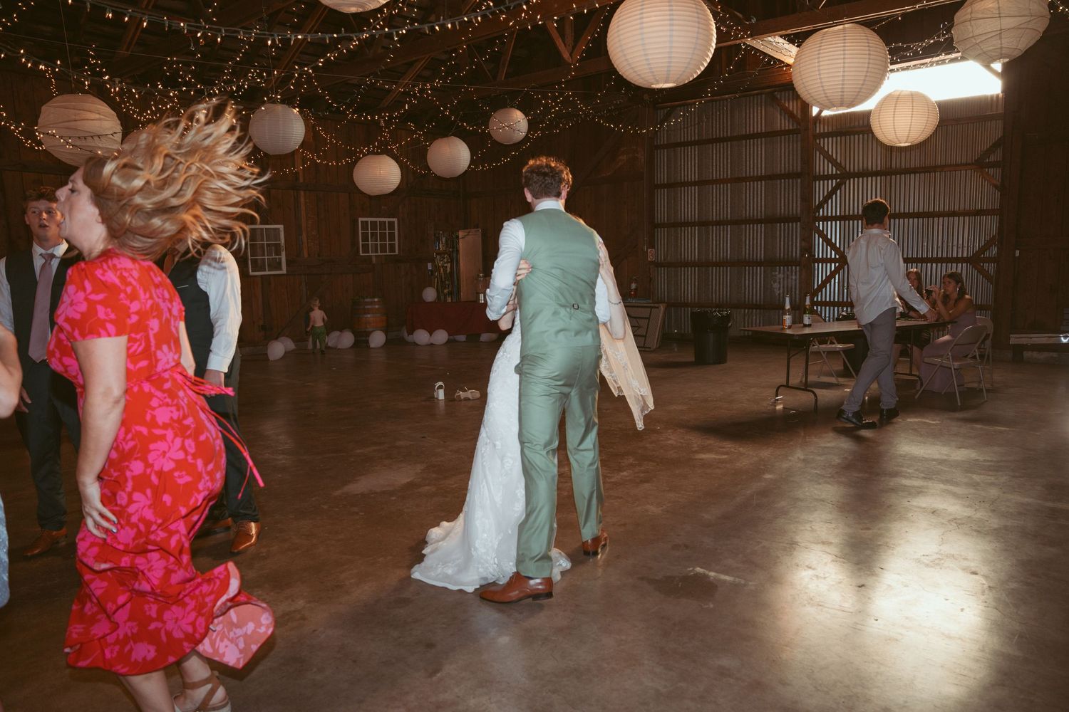 Wedding reception dance floor with guests in colorful attire under string lights.