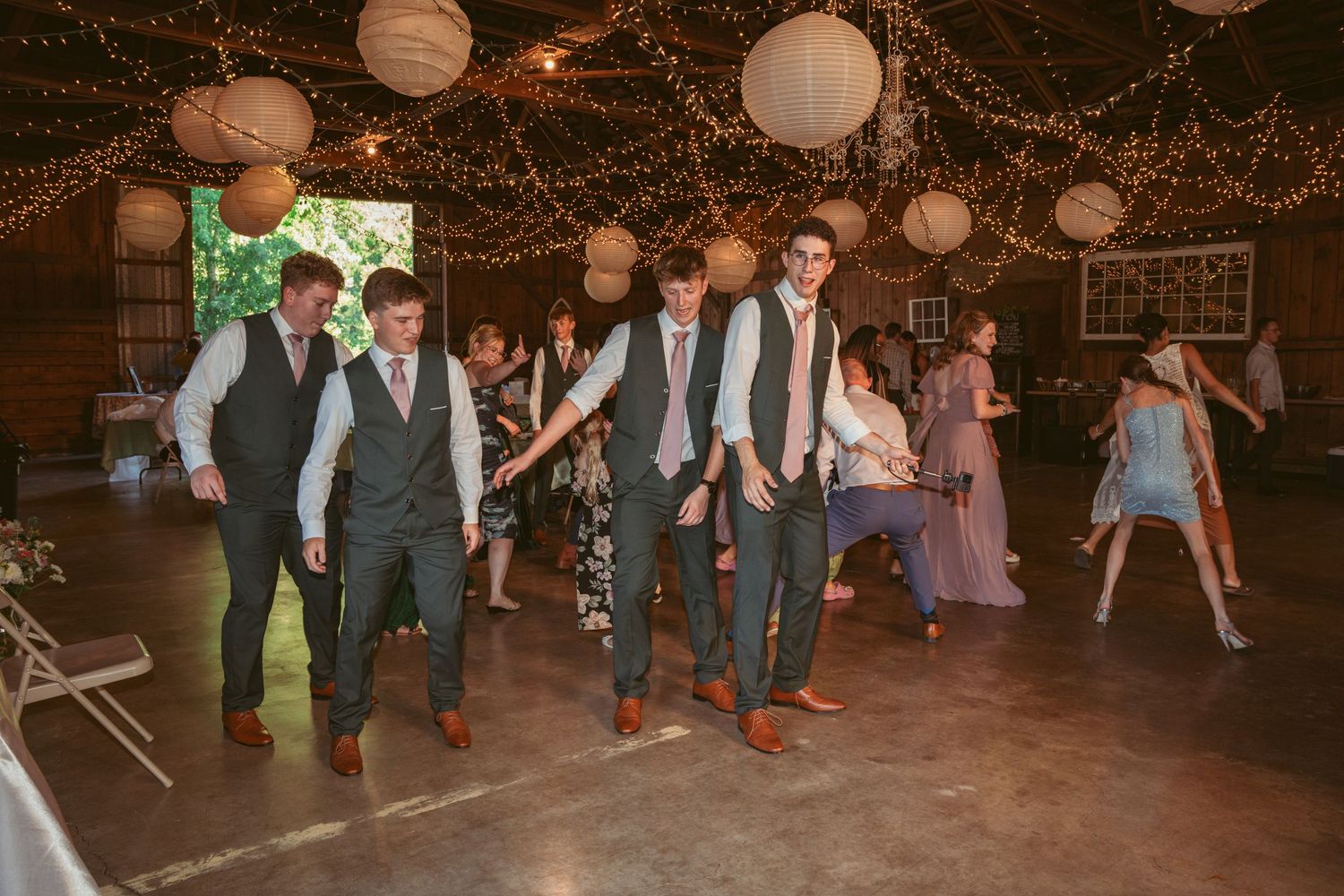 Group dance performance at a rustic barn wedding with string light decorations.