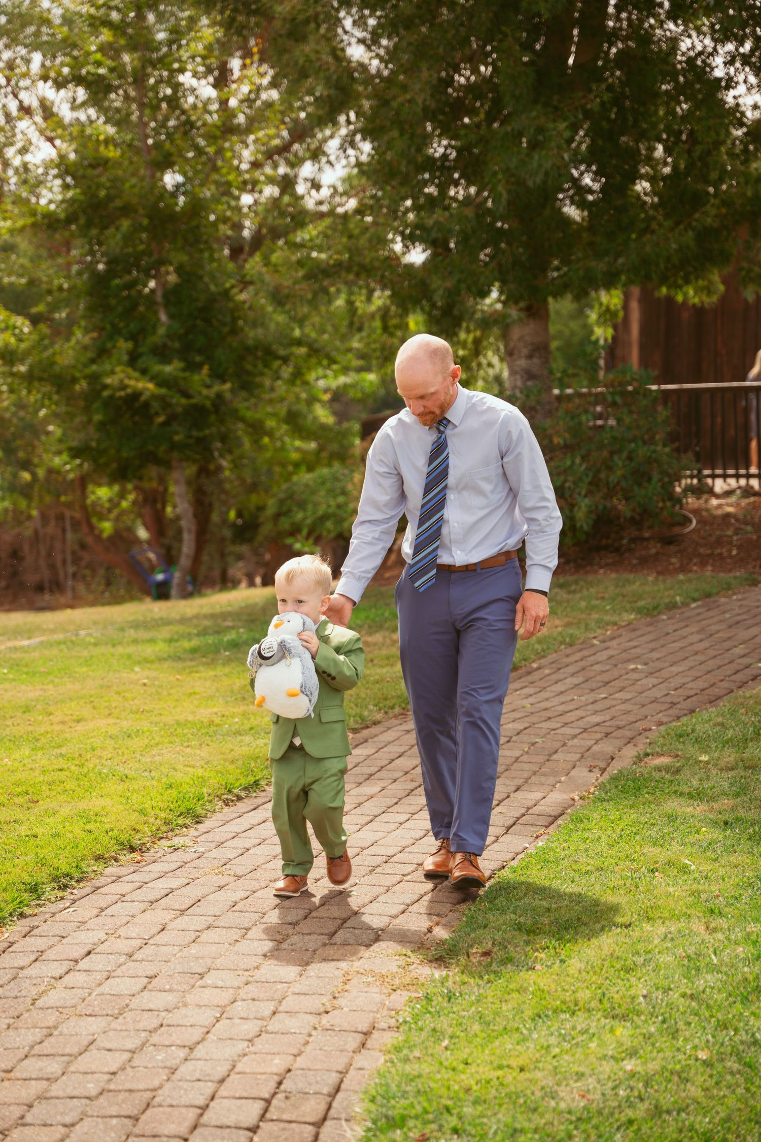 Adult and small child in formal wear walk hand-in-hand down brick pathway.