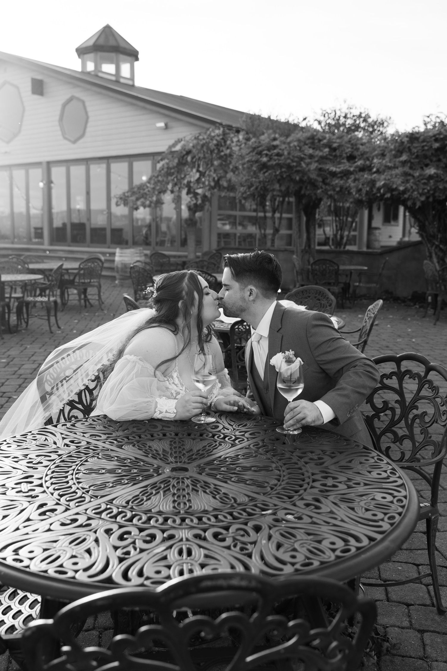 Black and white photo of a couple sharing an intimate moment at an ornate metal table outdoors.