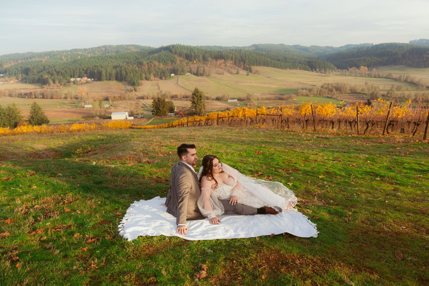Newlyweds share a romantic moment on a blanket in a scenic vineyard during golden hour.