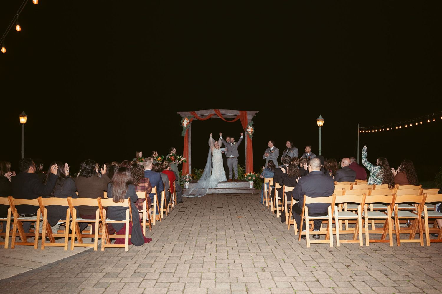 Guests seated at an evening outdoor wedding ceremony with string lights overhead.