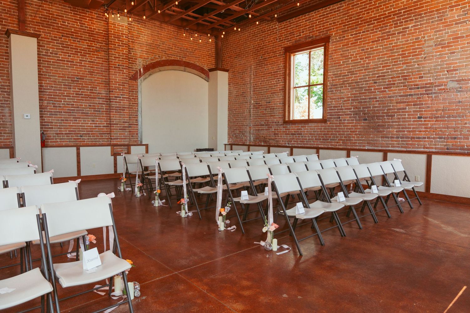 Rustic brick wall event venue with rows of white chairs arranged for a ceremony or presentation.