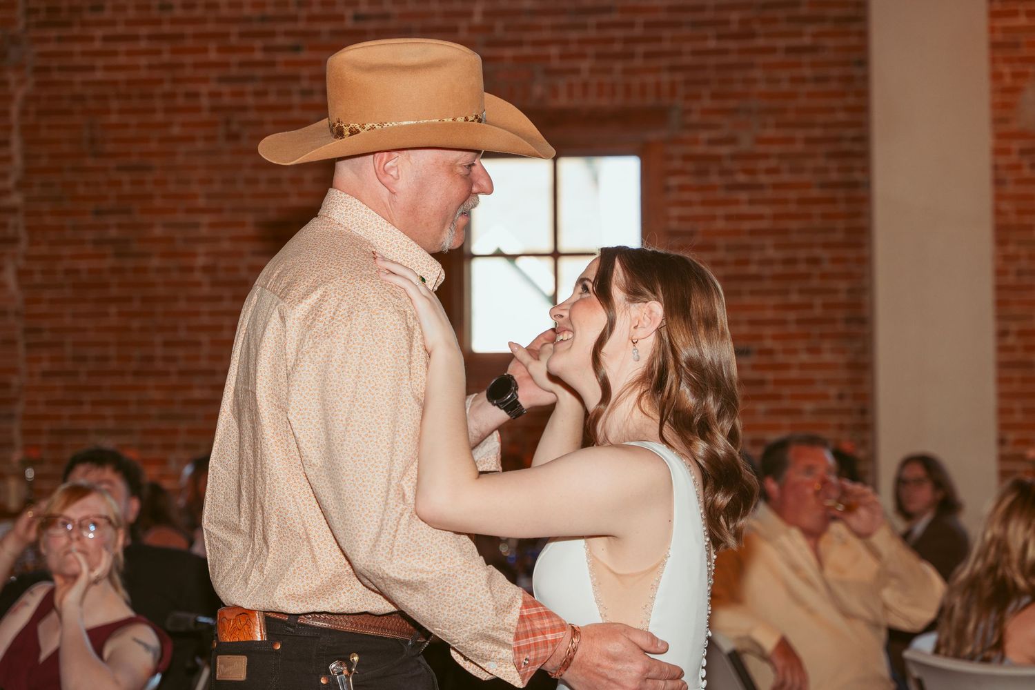 Couple dancing together in a rustic brick-walled venue with warm lighting.