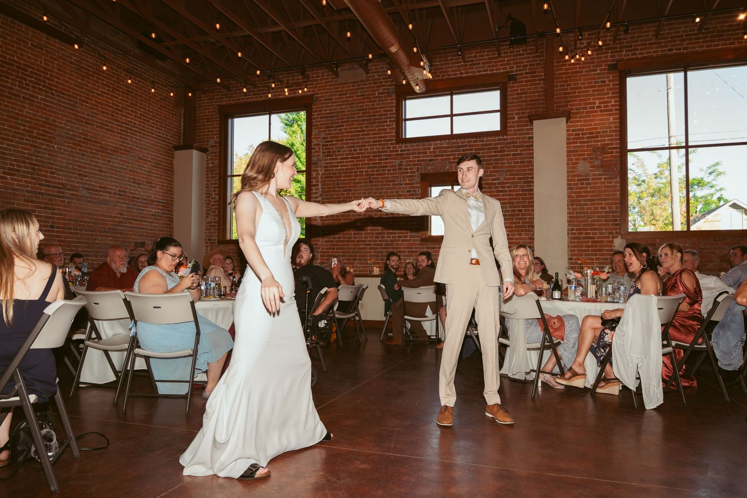 Wedding celebration in an industrial brick venue with twinkling lights overhead.