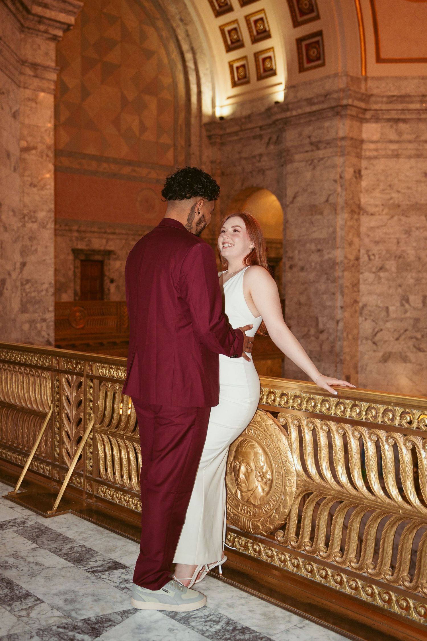 A romantic moment captured between a couple by an ornate gold railing in a historic building.