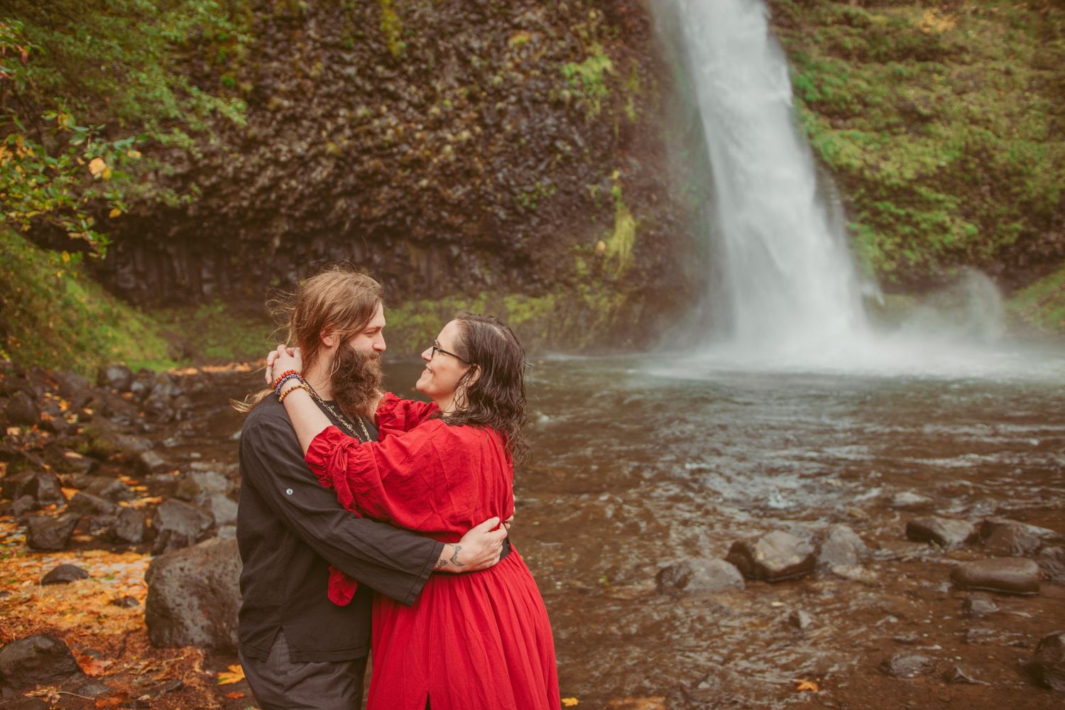 A waterfall creates a scenic backdrop for an intimate moment in an autumn forest.