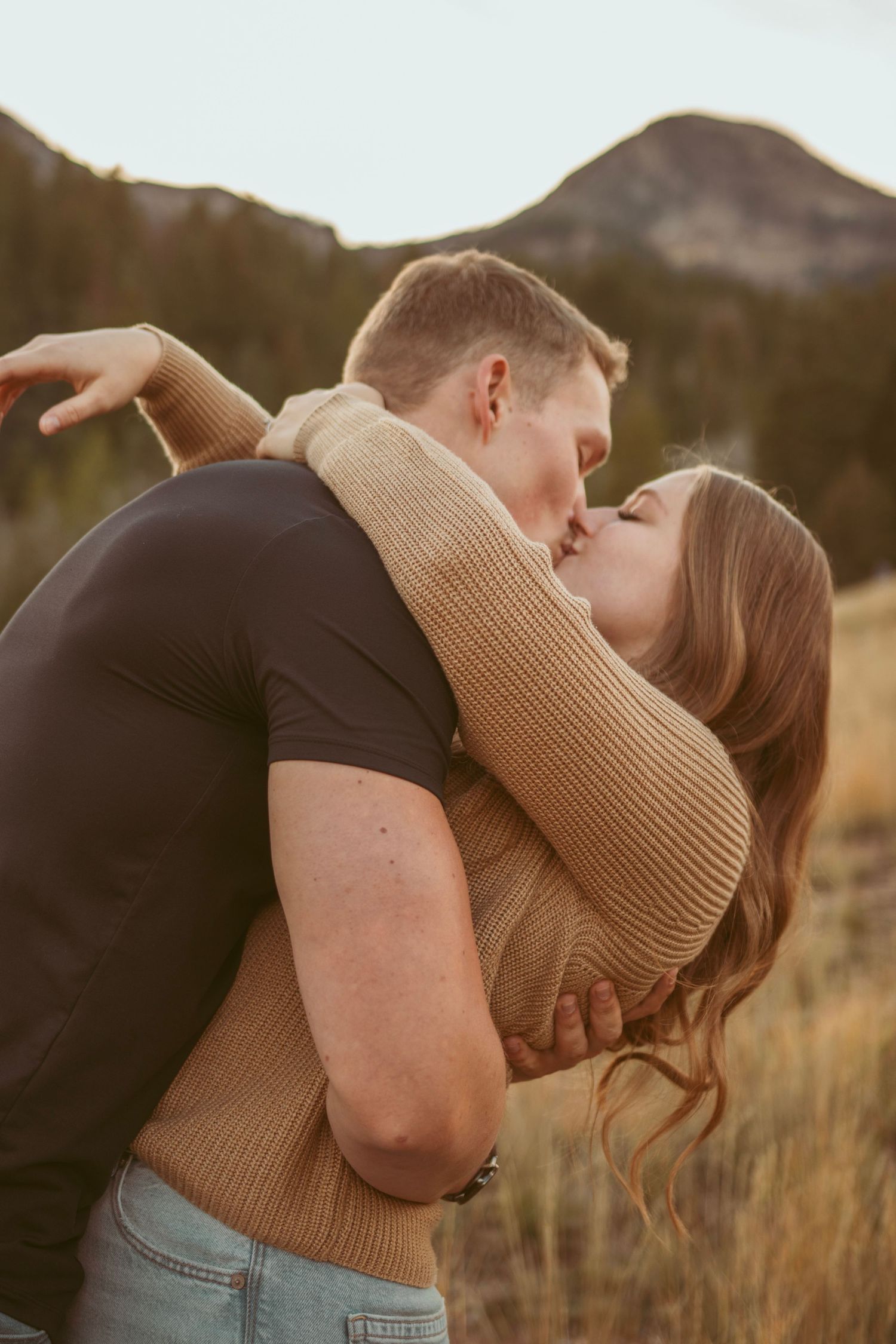 Romantic embrace in mountain meadow with warm sunset lighting.