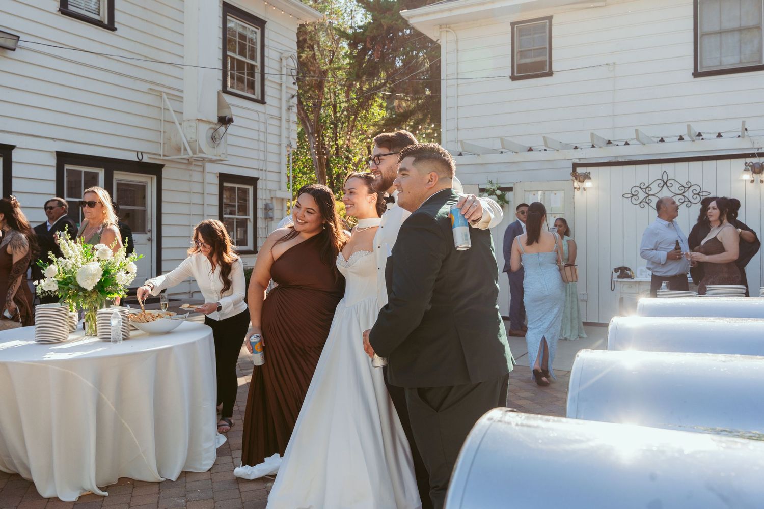 Elegant outdoor wedding reception setup with white tables and chairs against a white building.
