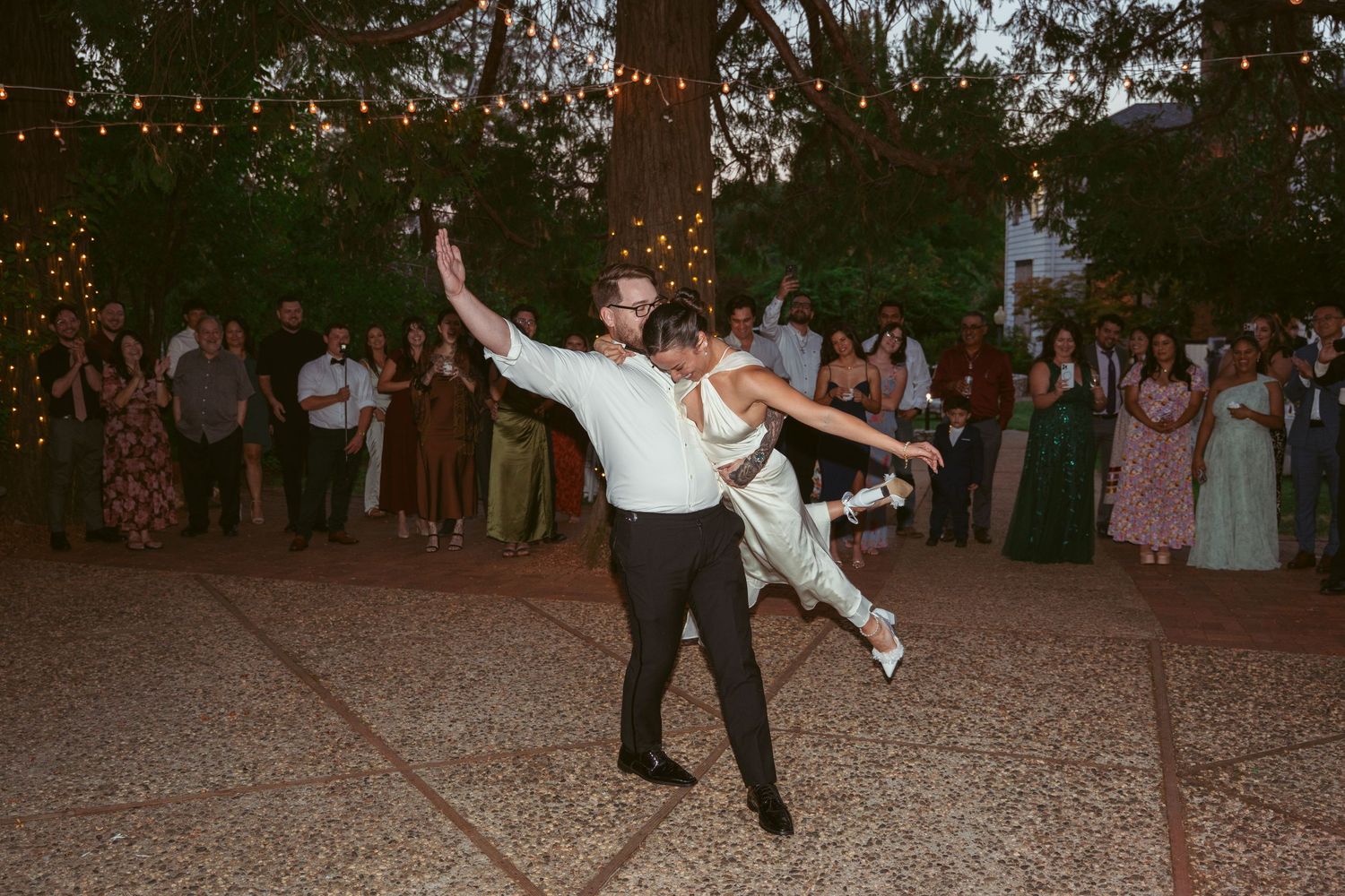 Couples dancing on a rustic outdoor dance floor under twinkling lights at a wedding reception.