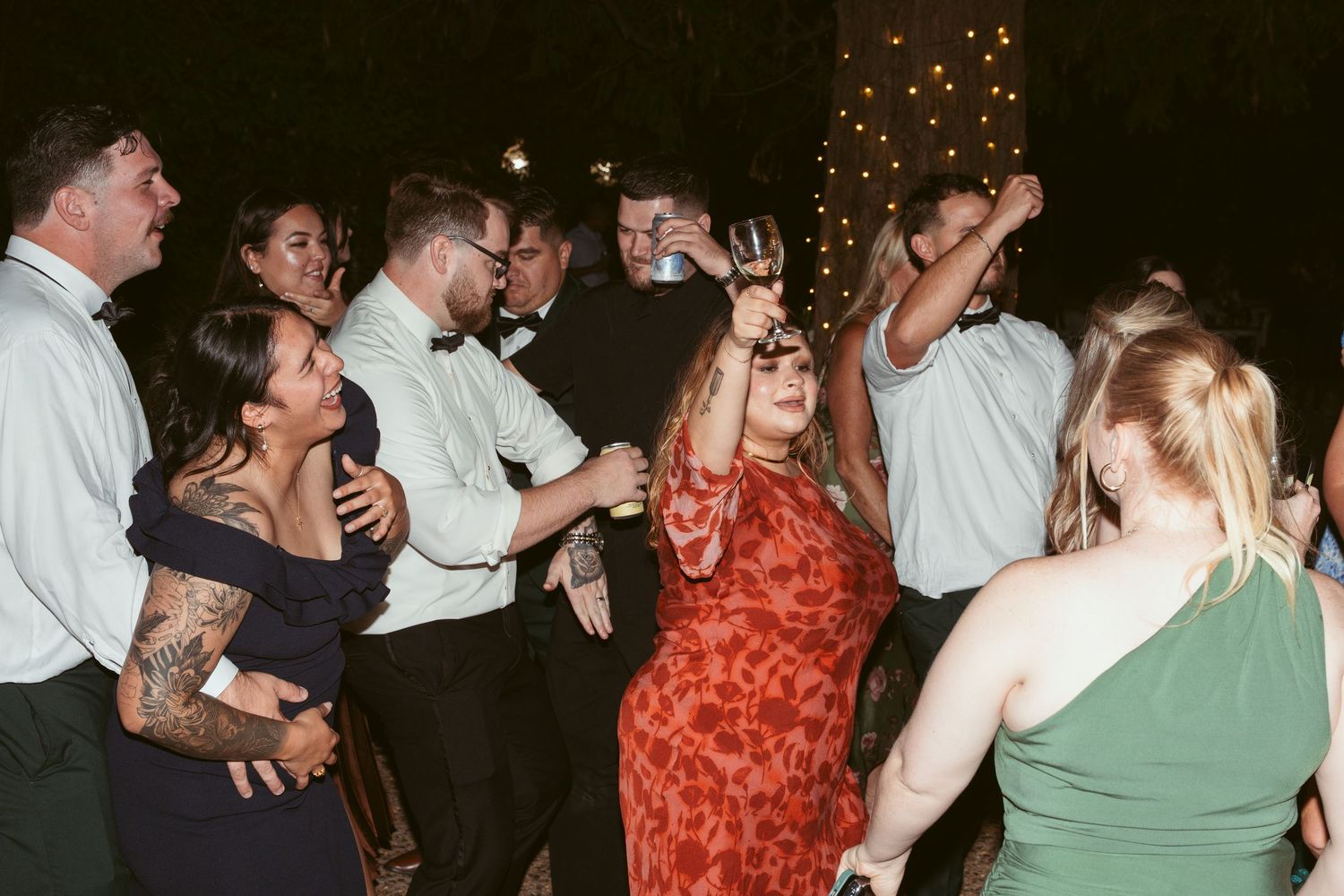 Wedding reception guests dance and celebrate under string lights in an outdoor venue.