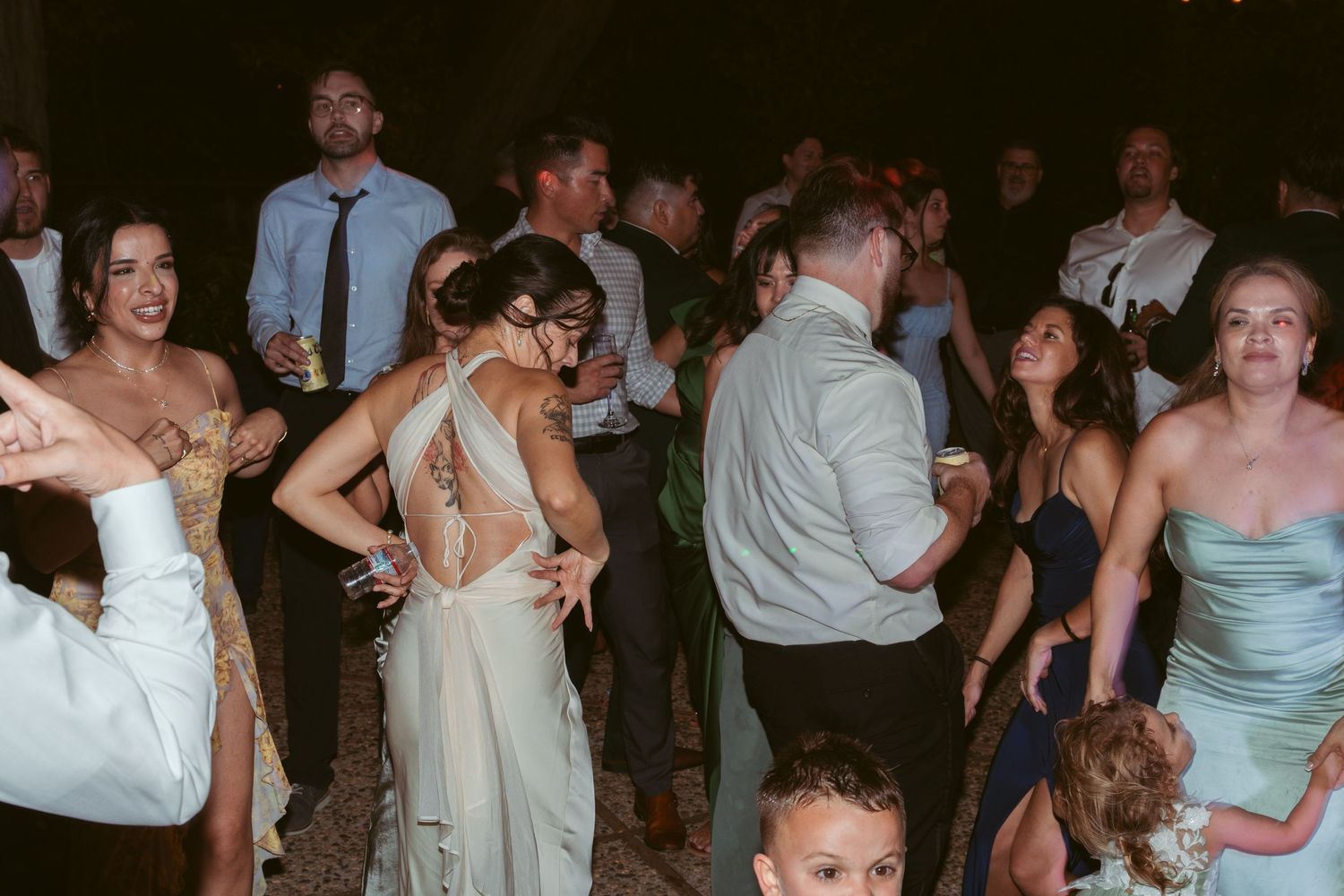 Wedding party dancing and celebrating at an evening reception with ambient lighting.