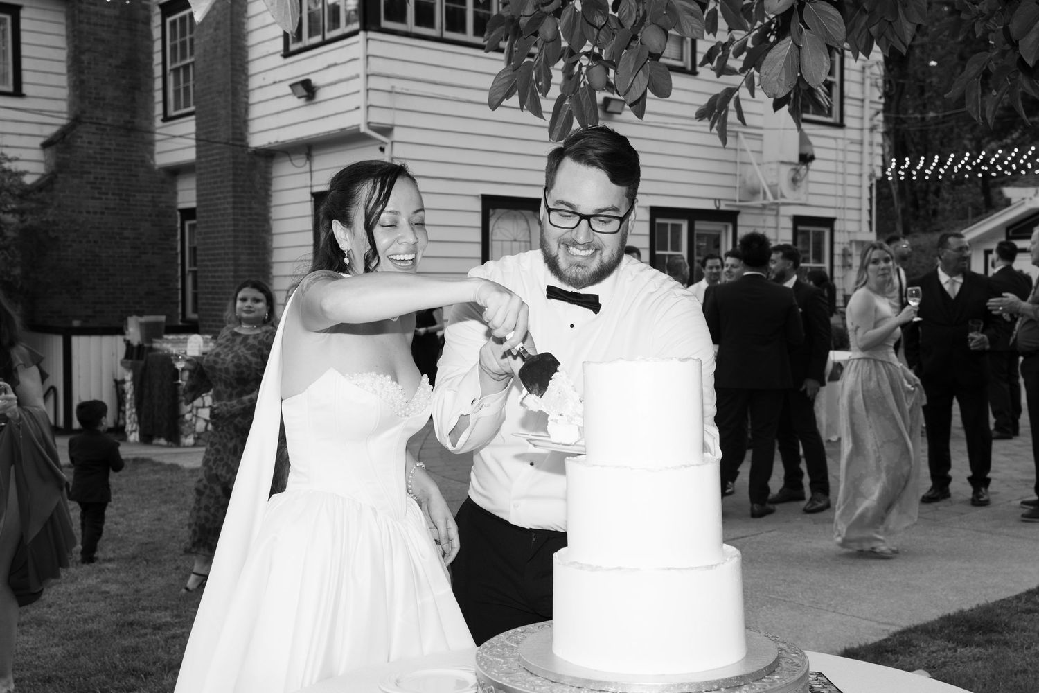 A couple enjoys a celebratory moment while cutting their wedding cake at an outdoor venue.