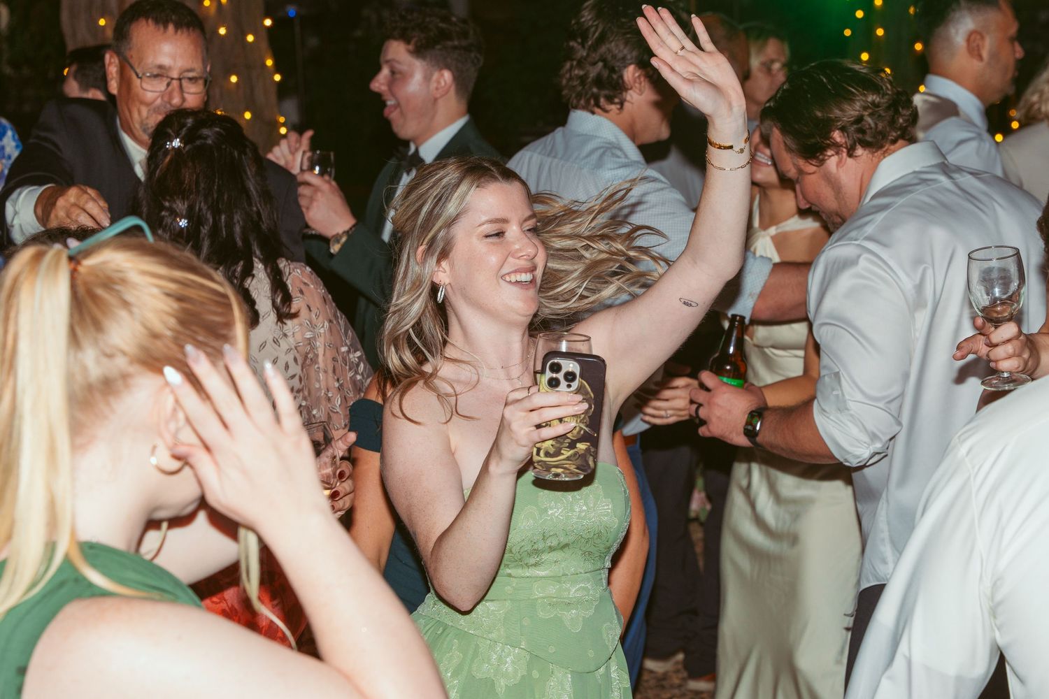 Wedding reception dance party with guests celebrating under string lights.