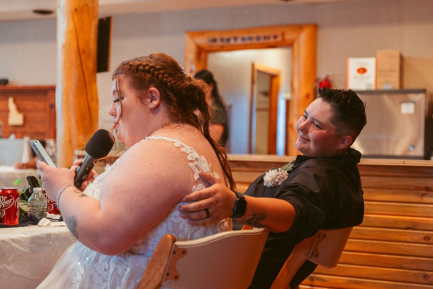 Couple sharing an emotional moment during wedding reception speeches at rustic wooden venue.