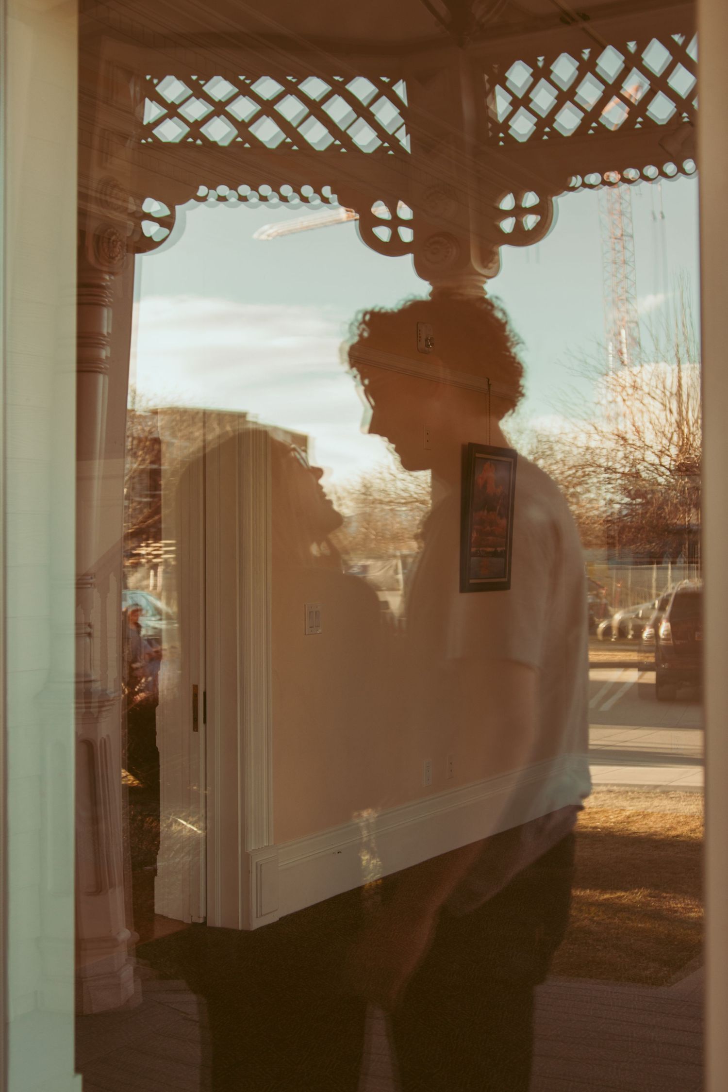 Silhouettes of two people reflected in a window pane with lattice patterns and outdoor scenery visible.