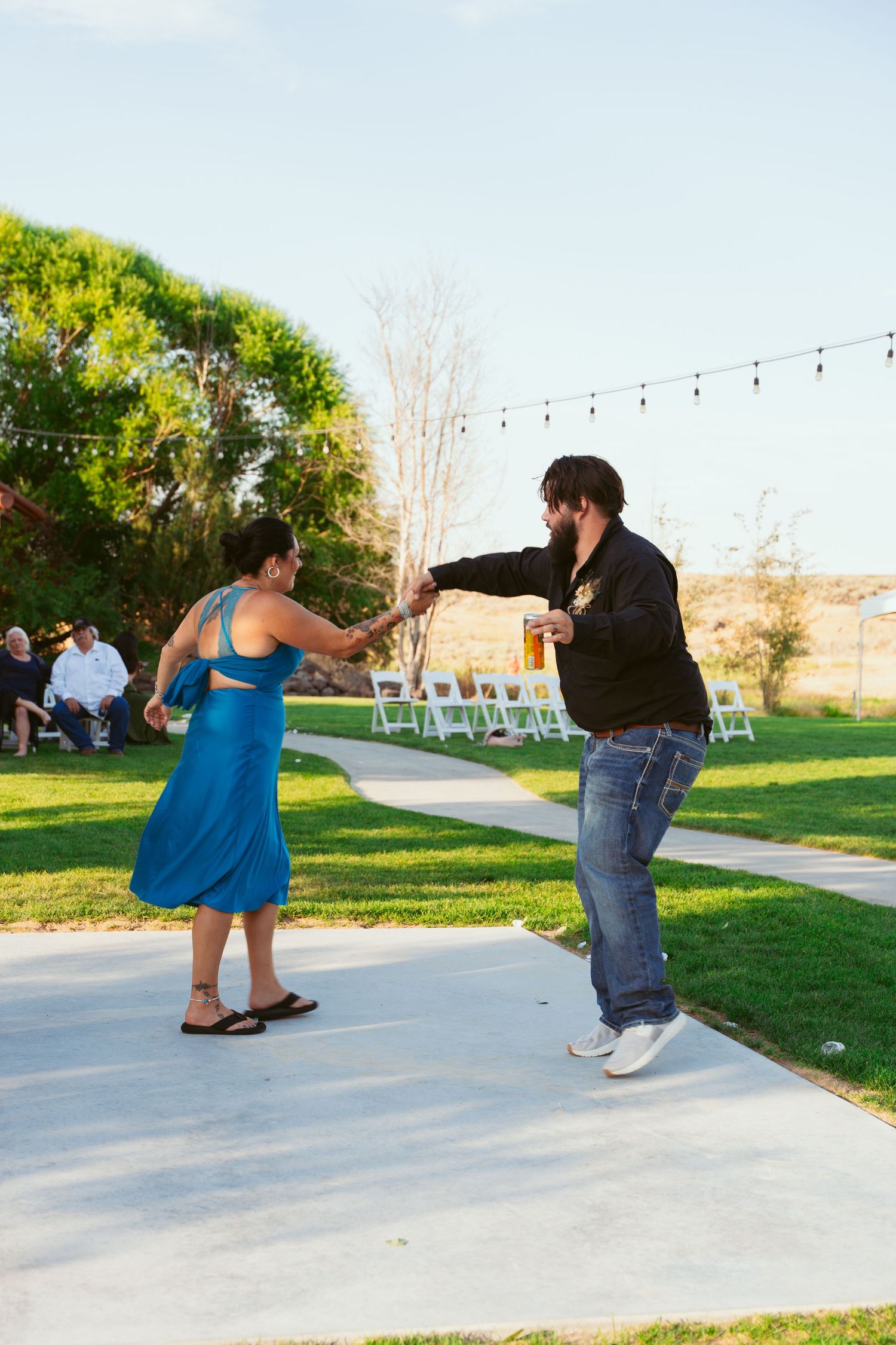 Dancers twirling on an outdoor dance floor with string lights and trees in the background.