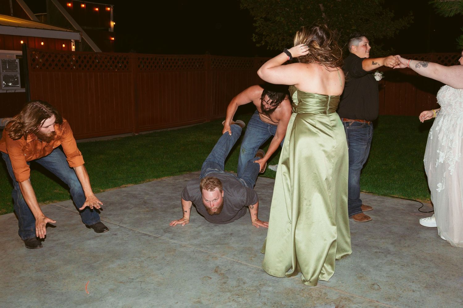 Wedding guests performing choreographed dance moves on an outdoor patio at night.