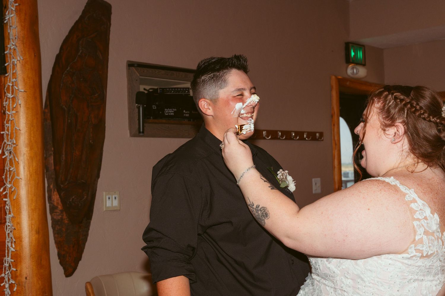 Couple laughing while smearing wedding cake on each other's faces during reception.