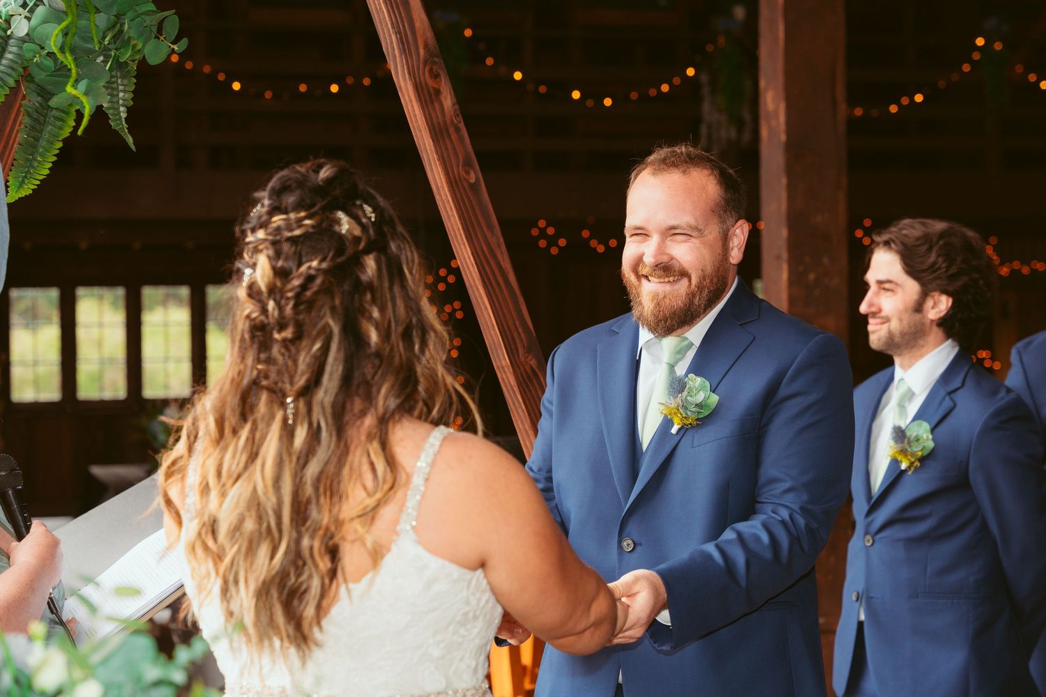 Wedding party in navy and white attire poses inside decorated barn venue.