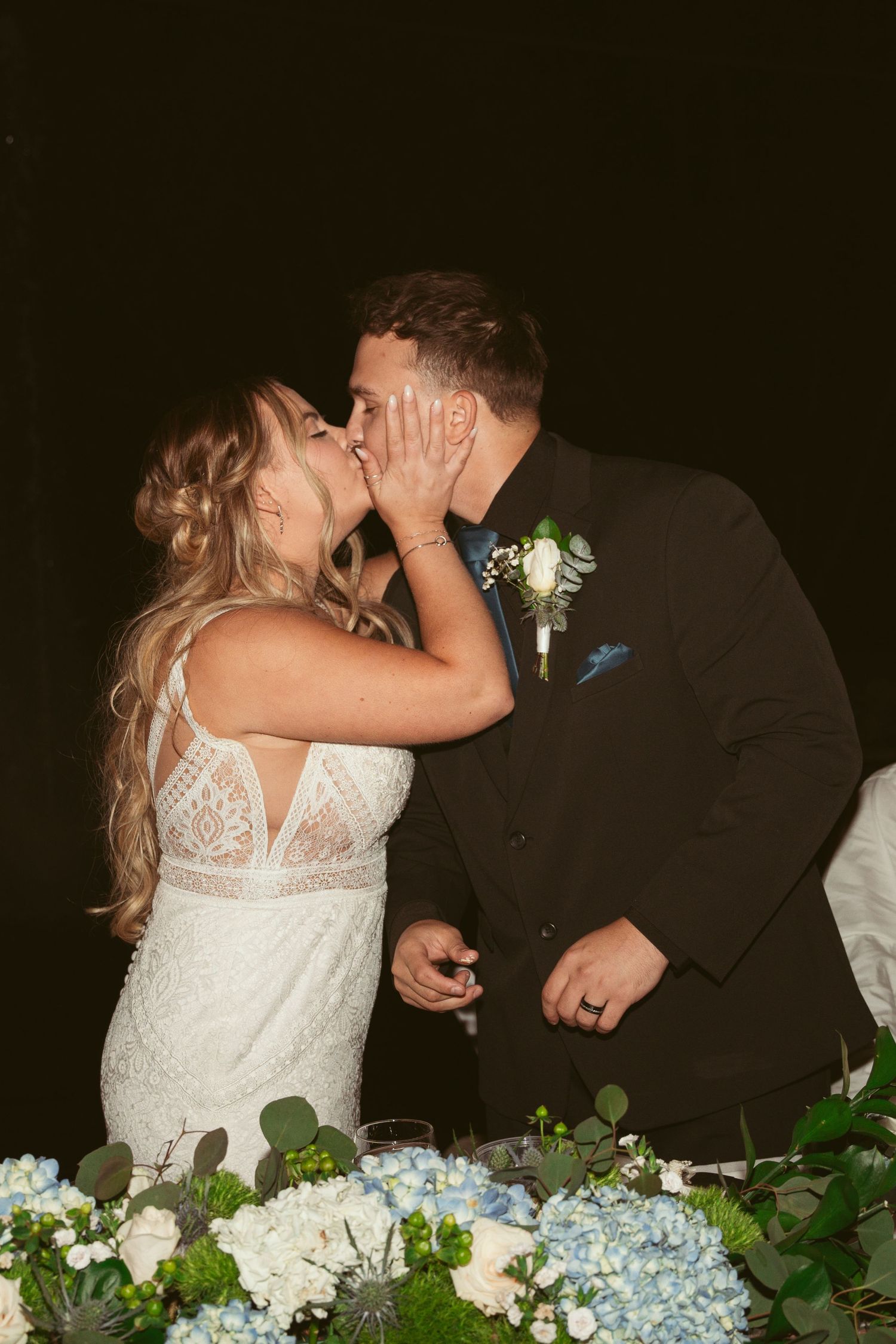 Couple shares an intimate moment at their wedding reception table with floral decorations.