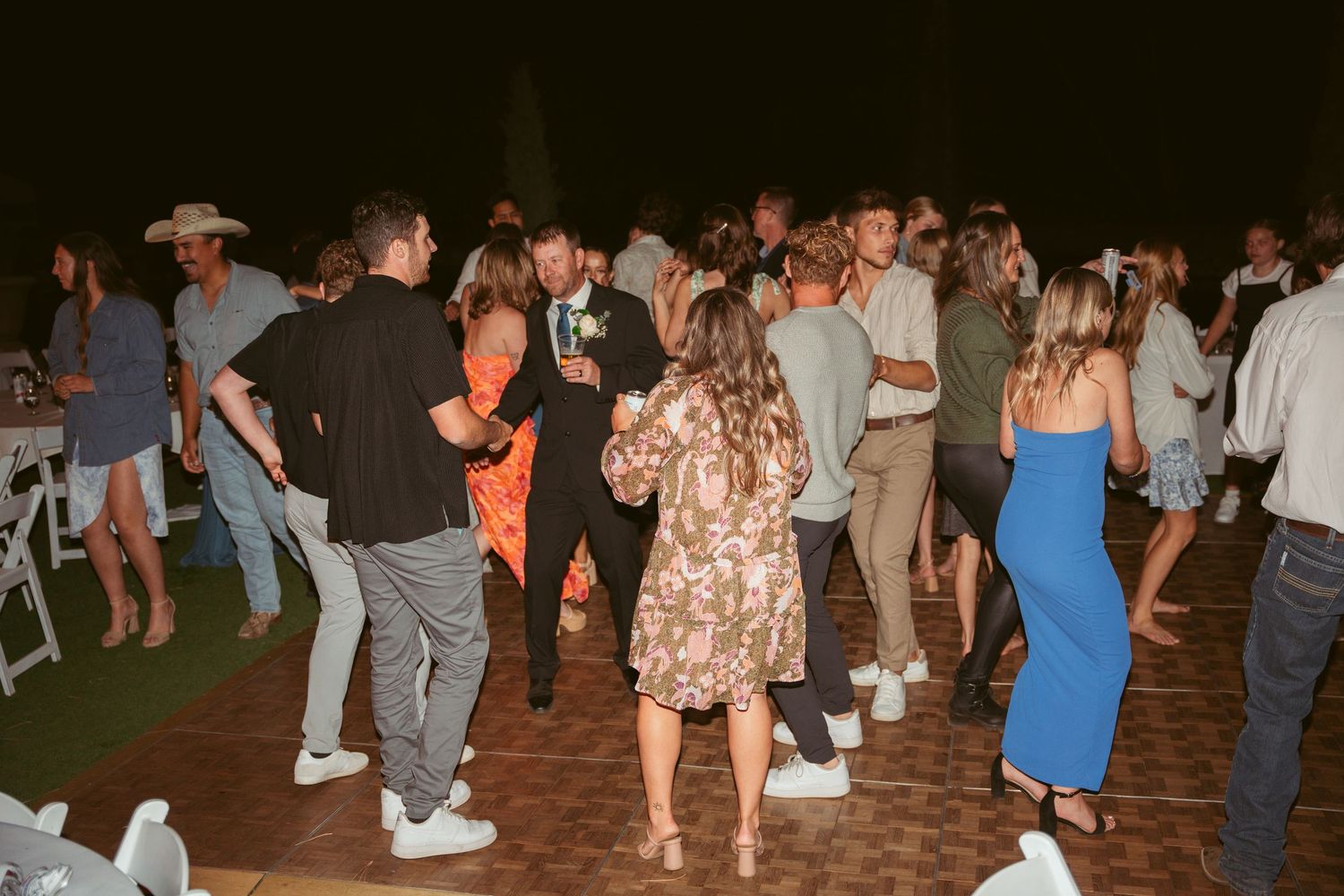 People dancing and socializing at a casual evening party with string light decorations.