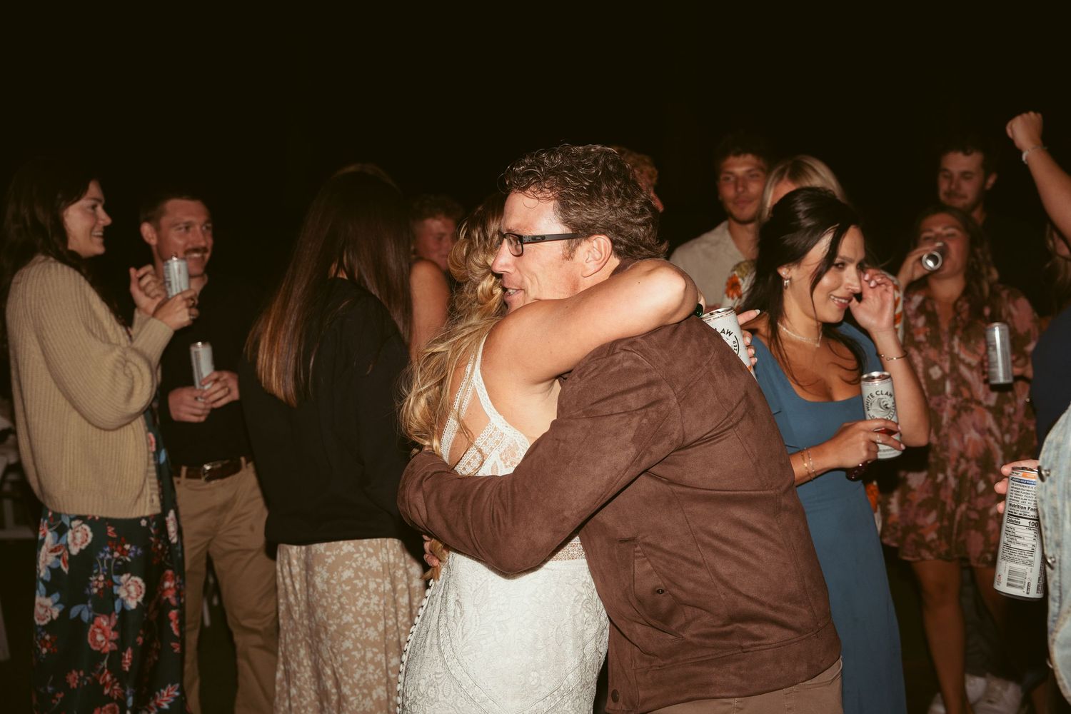 Guests embrace while dancing at an evening celebration under string lights.